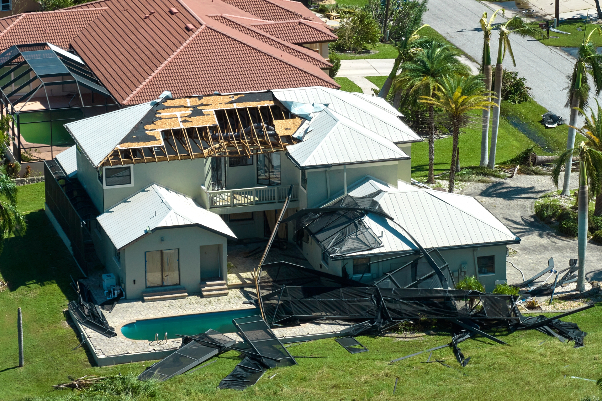 Aerial view of Florida home with severe hurricane damage — missing roof sections, destroyed pool enclosure, and debris scattered across the yard
