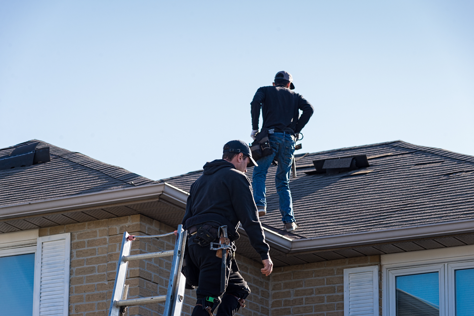 Two roofing contractors climbing onto a residential roof to perform an inspection in Tampa Bay